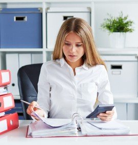 Beautiful business woman calculates tax at desk in office