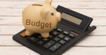 Making a Budget, A golden piggy bank and calculator on a wood background with text Budget
