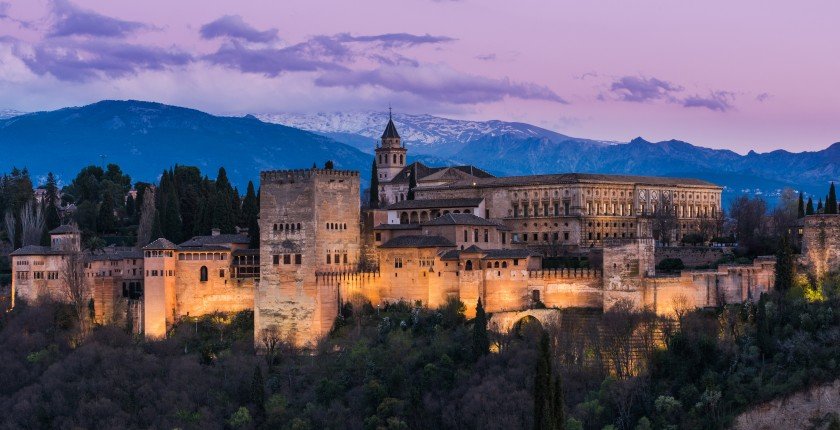 Illuminated Arabic Alhambra palace in Granada,Spain with Sierra Nevada snowy mountains in background