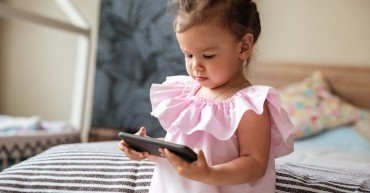Image of serious little girl child indoors using mobile phone. Looking aside.