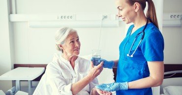 medicine, age, health care and people concept - nurse giving medication and glass of water to senior woman at hospital ward