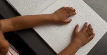 High angle view of mixed-race blind schoolboy hands reading a braille book in classroom at elementary school