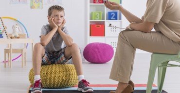 Small boy sitting on a pouf, talking with a psychotherapist
