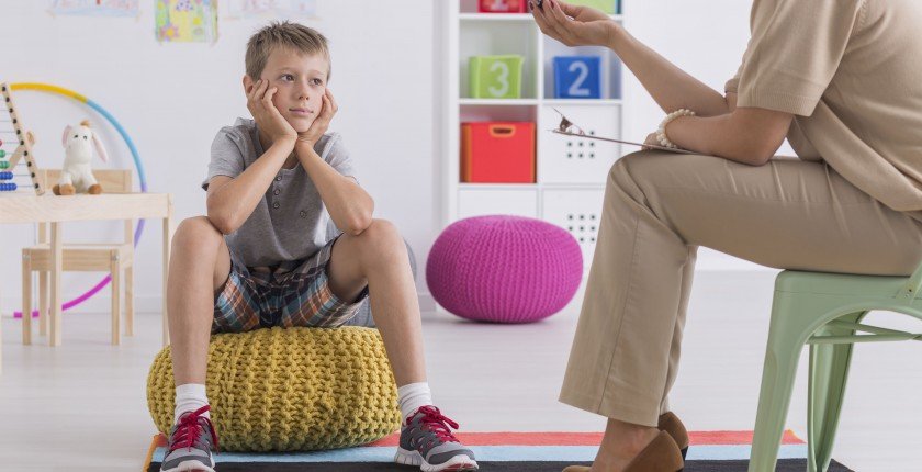 Small boy sitting on a pouf, talking with a psychotherapist