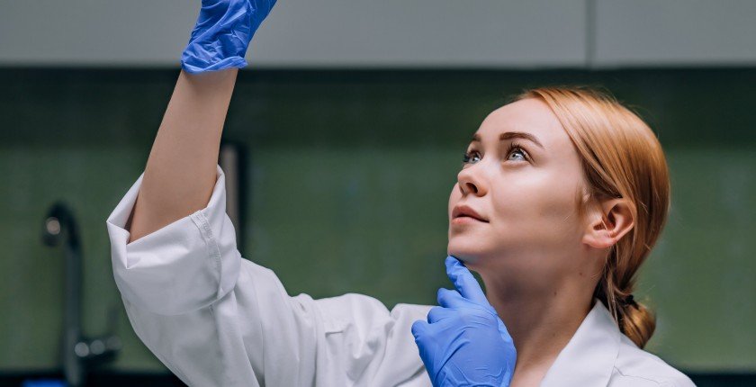 Female medical or scientific researcher or woman doctor looking at a test tube of clear solution in a laboratory.