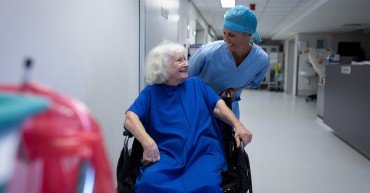 Front view of a Caucasian female surgeon talking with a Caucasian senior female patient sitting in a wheelchair in hospital corridor